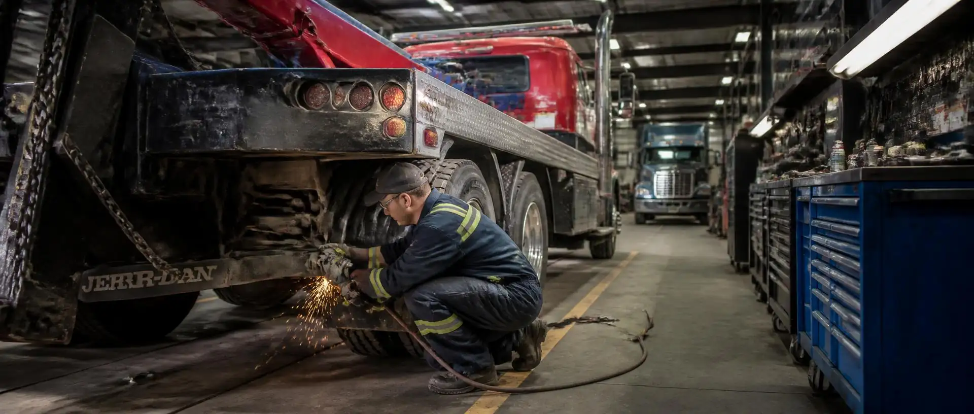 Mechanic grinding and repairing the frame of a heavy duty tow truck in a repair shop